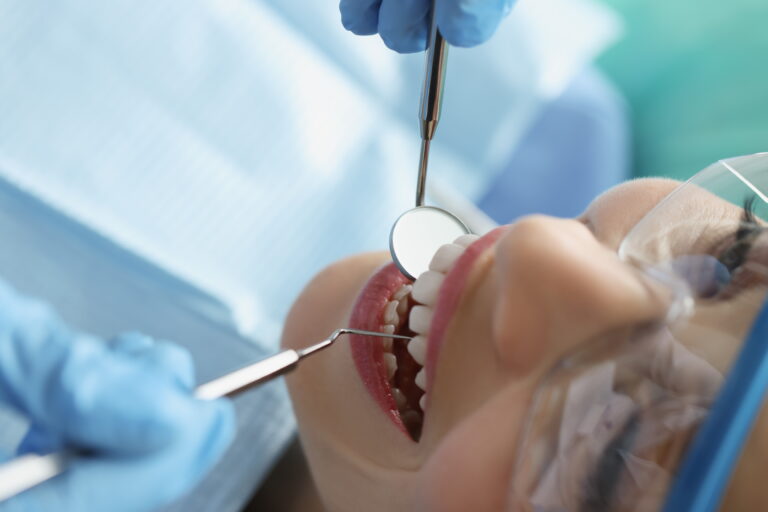 dentist in protective gloves examining teeth of female patient using metal instruments in clinic closeup